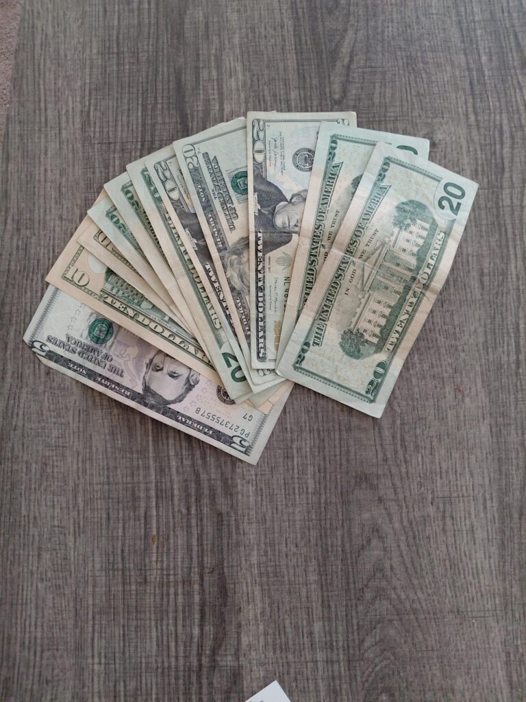 A fan of assorted US dollar bills spread on a wooden surface.